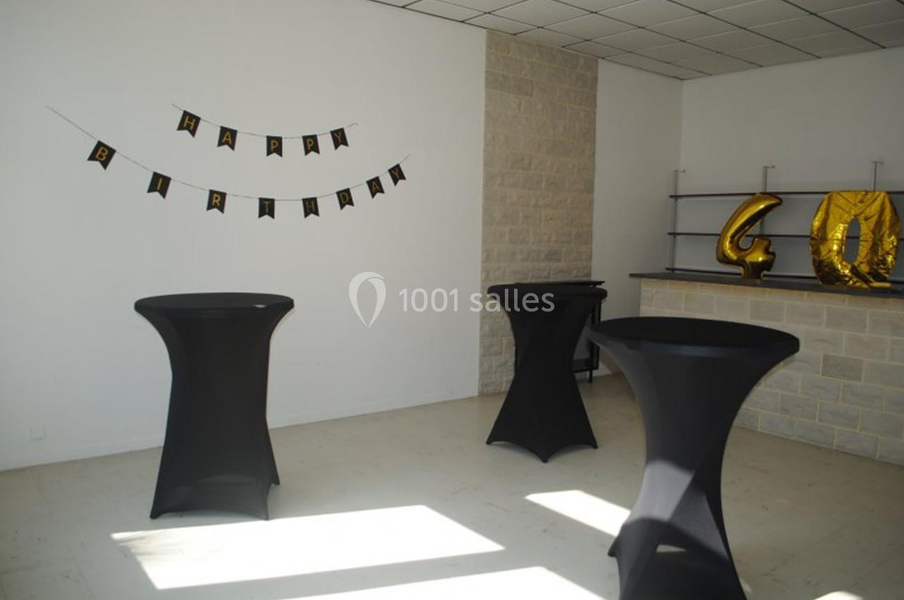 Salle décorée pour un anniversaire avec guirlande ’Happy Birthday’, ballons dorés ’40’ et tables hautes noires.