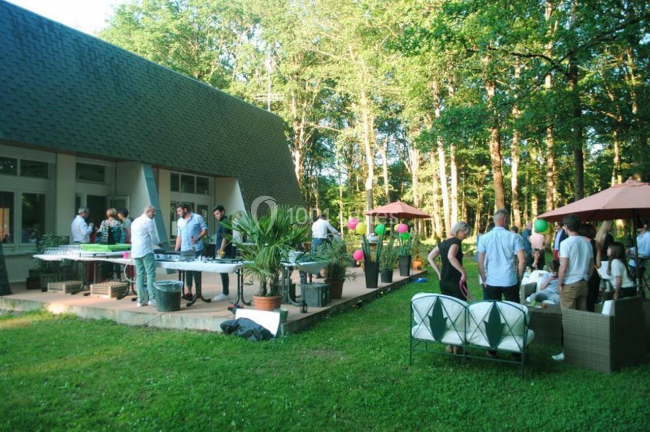Groupe de personnes réunies sur une terrasse ensoleillée entourée de verdure, avec tables et parasols.