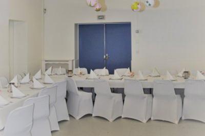 Salle décorée avec des ballons bleus, blancs et dorés, tables dressées et groupe de personnes discutant debout.