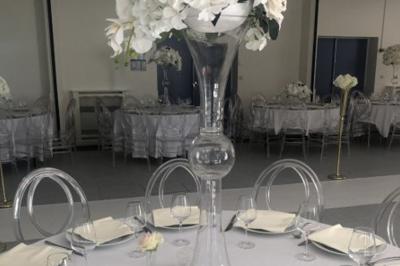 Salle décorée avec des ballons bleus, blancs et dorés, tables dressées et groupe de personnes discutant debout.
