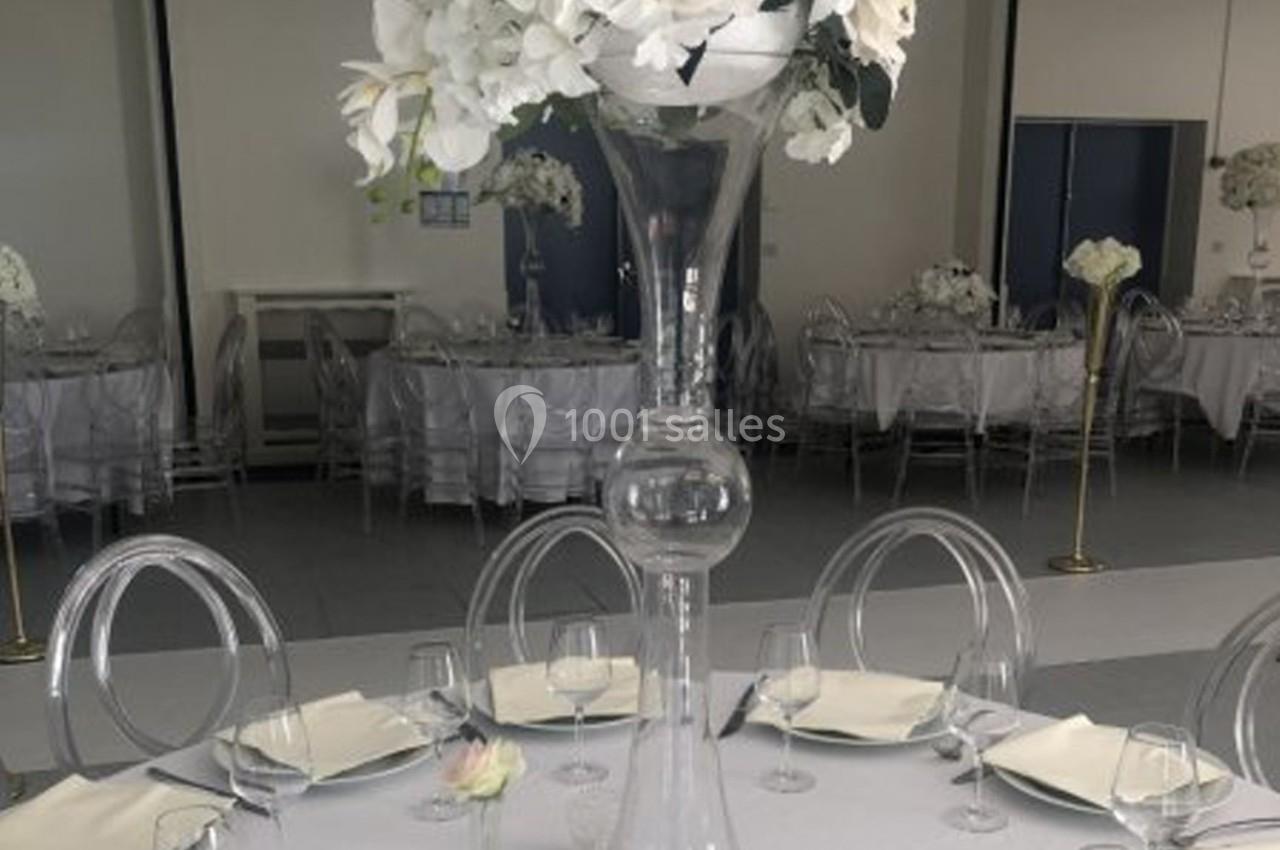 Table de réception élégante avec nappes blanches, chaises transparentes et centre de table floral avec des orchidées…