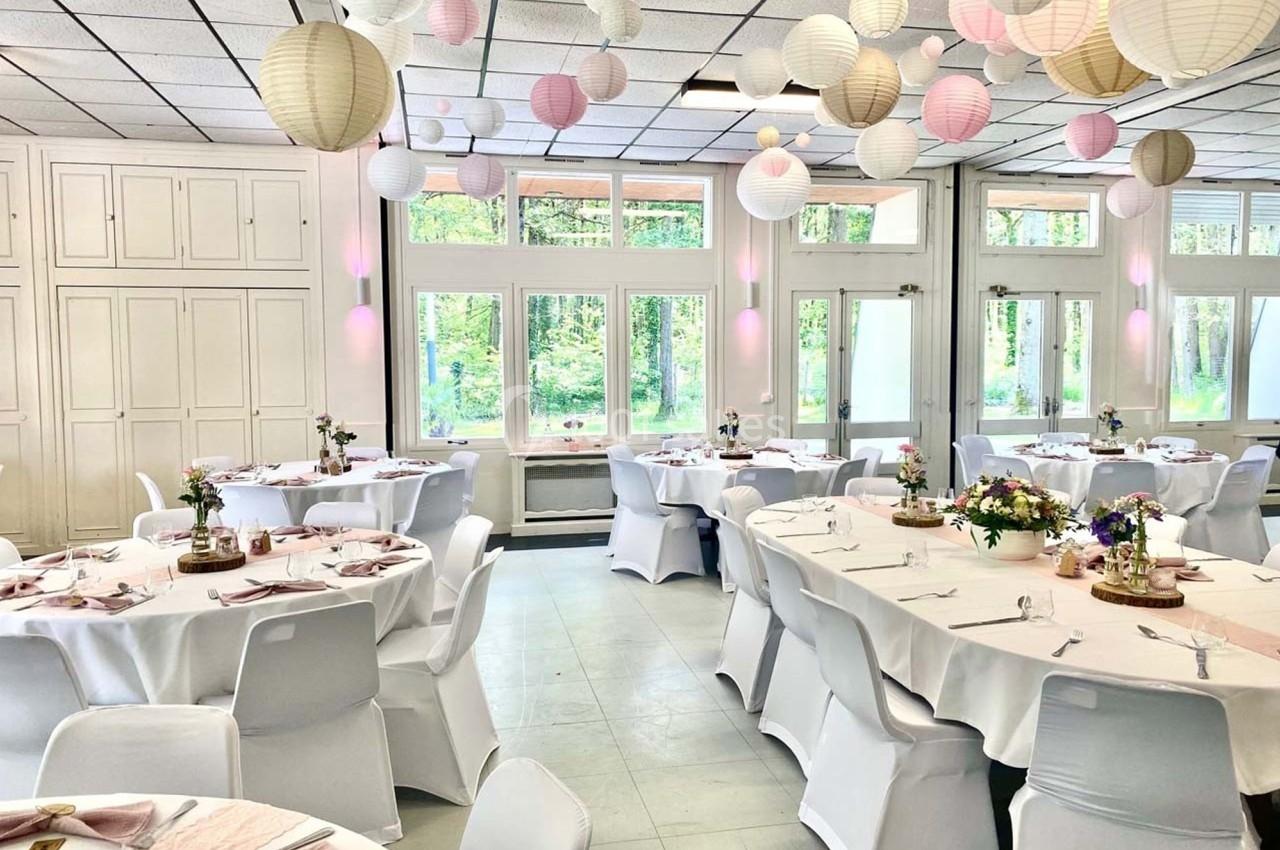 Salle de réception décorée de lanternes suspendues, tables rondes dressées avec nappes blanches et arrangements floraux.