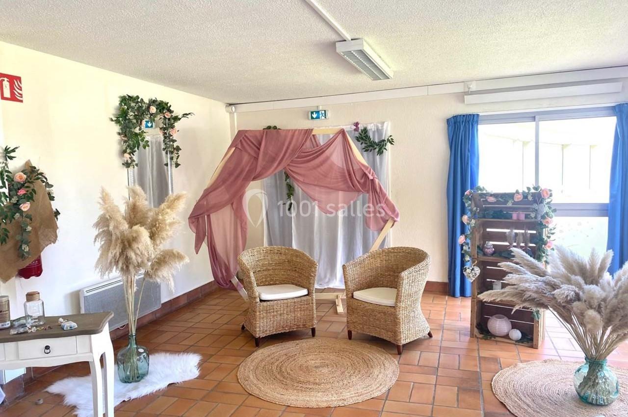 Espace décoré avec des fauteuils en rotin, des voilages roses, des plantes et des pampas sur un sol en carrelage.