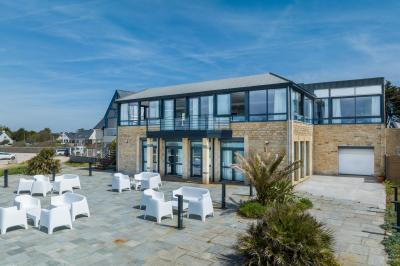 Vue aérienne d'une plage bordée de falaises avec des maisons et un parking à proximité, dans un paysage côtier.