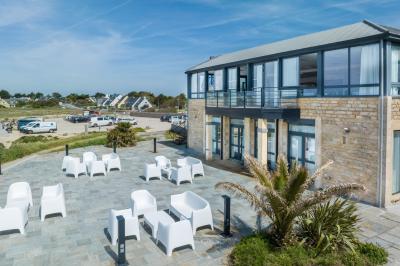 Vue aérienne d'une plage bordée de falaises avec des maisons et un parking à proximité, dans un paysage côtier.