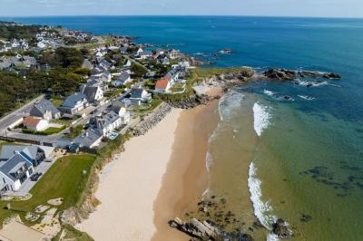 Vue aérienne d'une plage bordée de falaises avec des maisons et un parking à proximité, dans un paysage côtier.