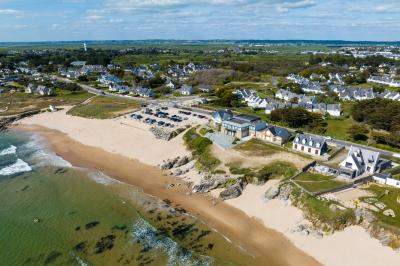 Vue aérienne d'une plage bordée de falaises avec des maisons et un parking à proximité, dans un paysage côtier.