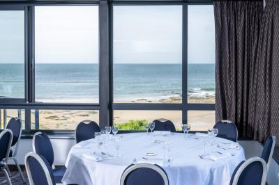 Vue aérienne d'une plage bordée de falaises avec des maisons et un parking à proximité, dans un paysage côtier.