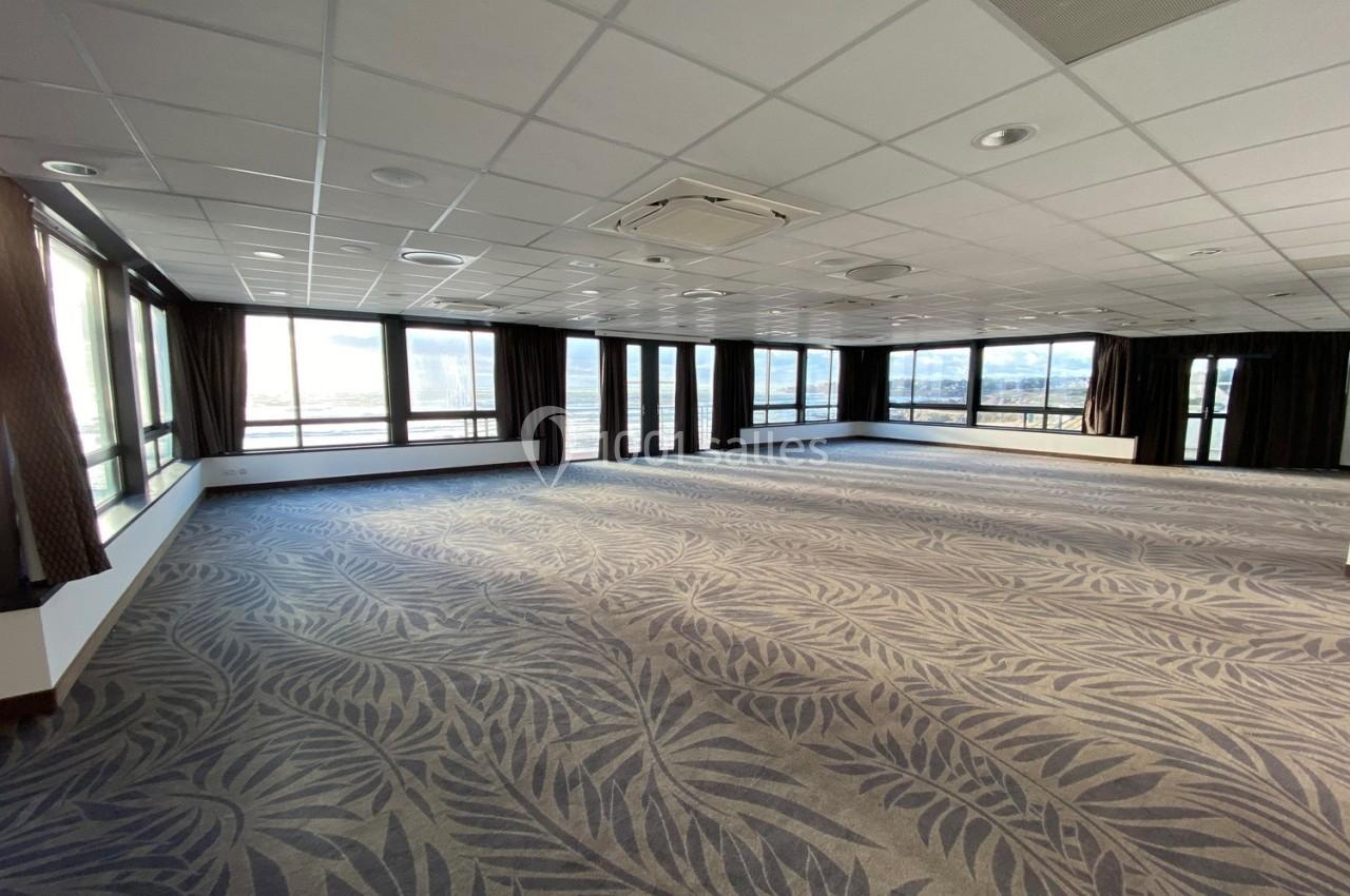 Salle spacieuse et lumineuse avec moquette à motifs, grandes fenêtres et plafond à dalles blanches.