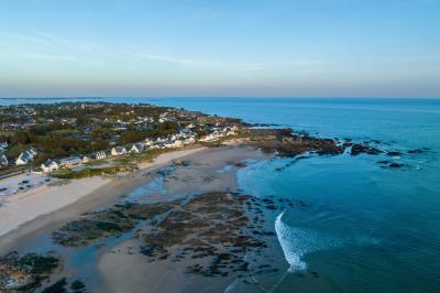 Vue aérienne d'une plage bordée de falaises avec des maisons et un parking à proximité, dans un paysage côtier.