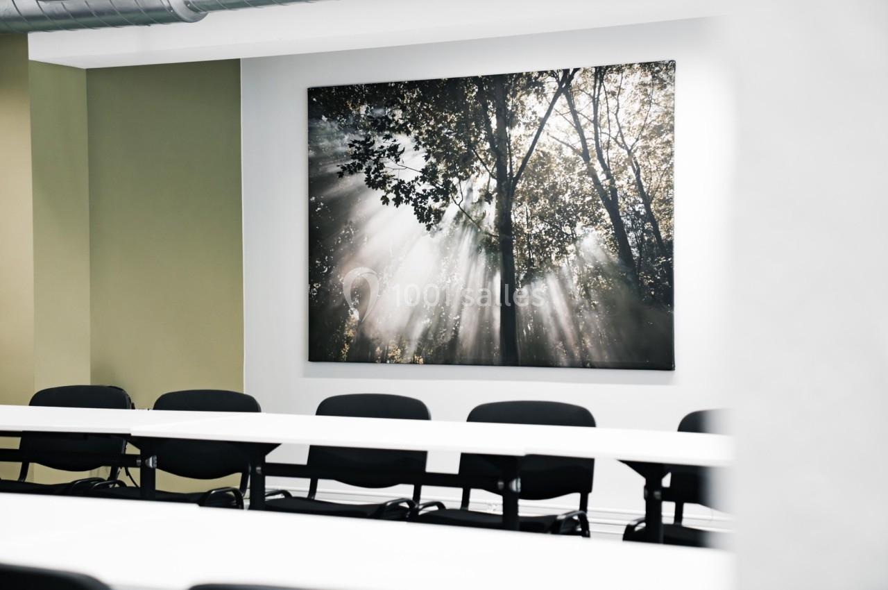 Salle de réunion avec des chaises noires et un tableau mural représentant des rayons de soleil à travers des arbres.