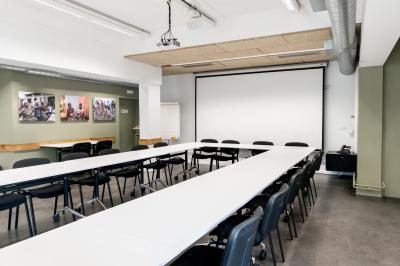 Personnes assises à des tables sur une terrasse en bois, entourée de verdure et d'immeubles modernes en arrière-plan.