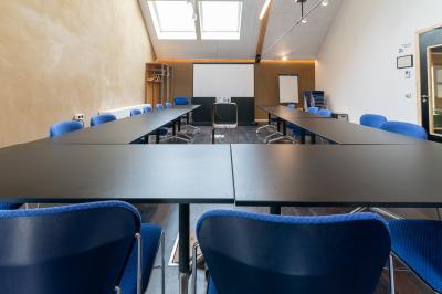 Bâtiment moderne avec façade en verre et briques, entouré de végétation et d'une allée pavée.