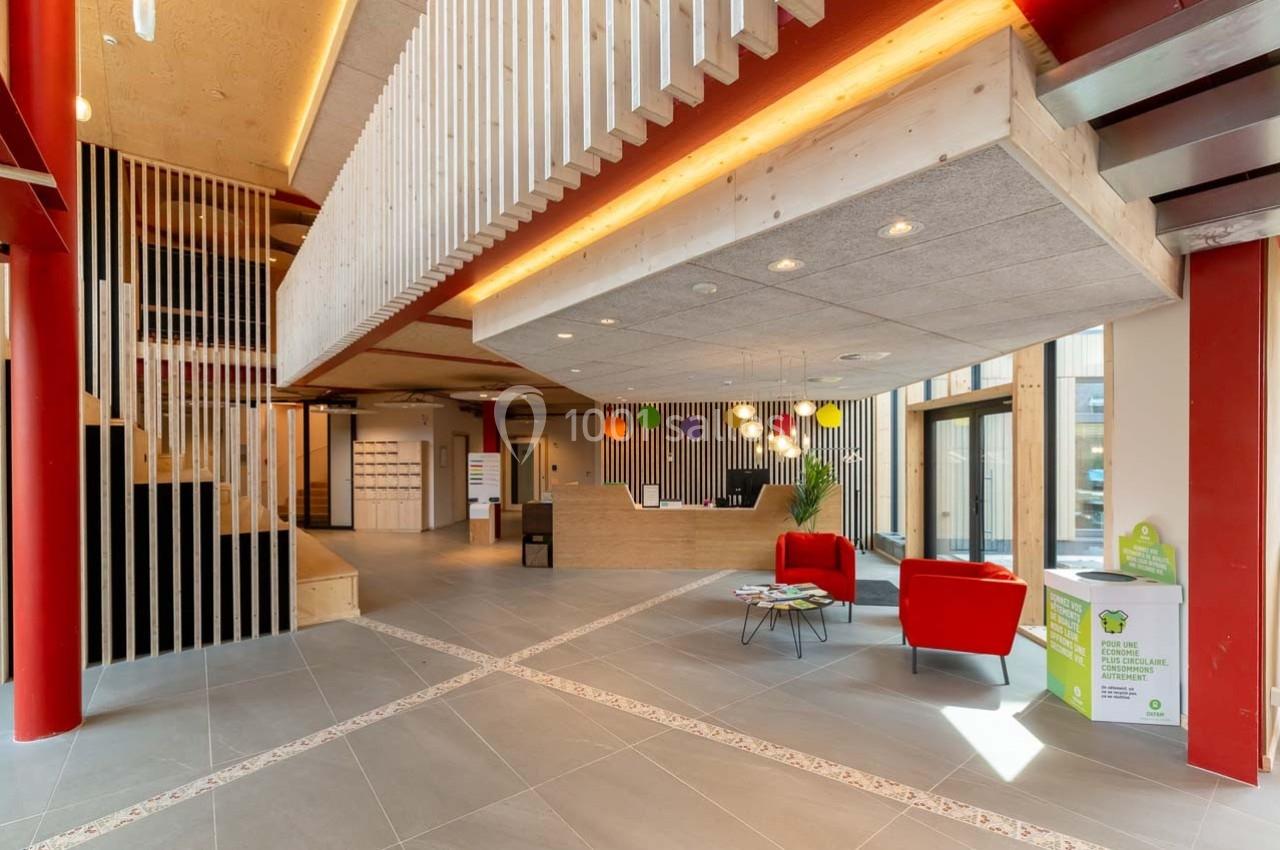 Hall d'accueil moderne avec comptoir en bois, fauteuils rouges, éclairage chaleureux et éléments décoratifs en bois.