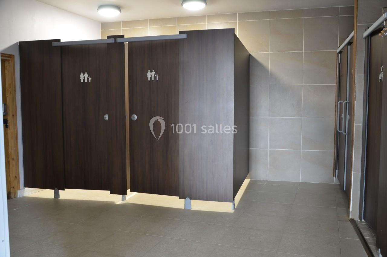 Cabines de toilettes en bois sombre avec icônes homme et femme, dans un espace carrelé et bien éclairé.