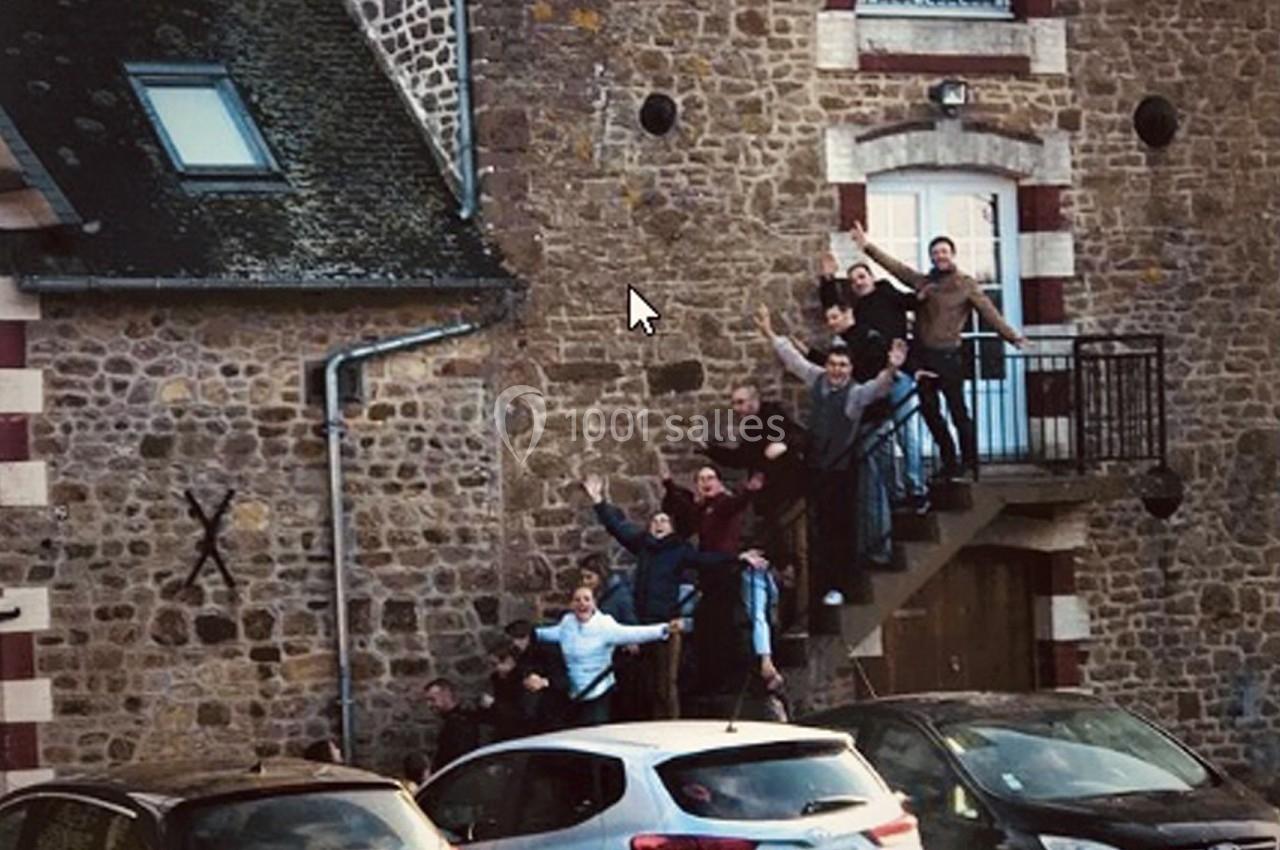 Un groupe de personnes pose sur un escalier extérieur en pierre devant un bâtiment ancien avec des voitures garées.