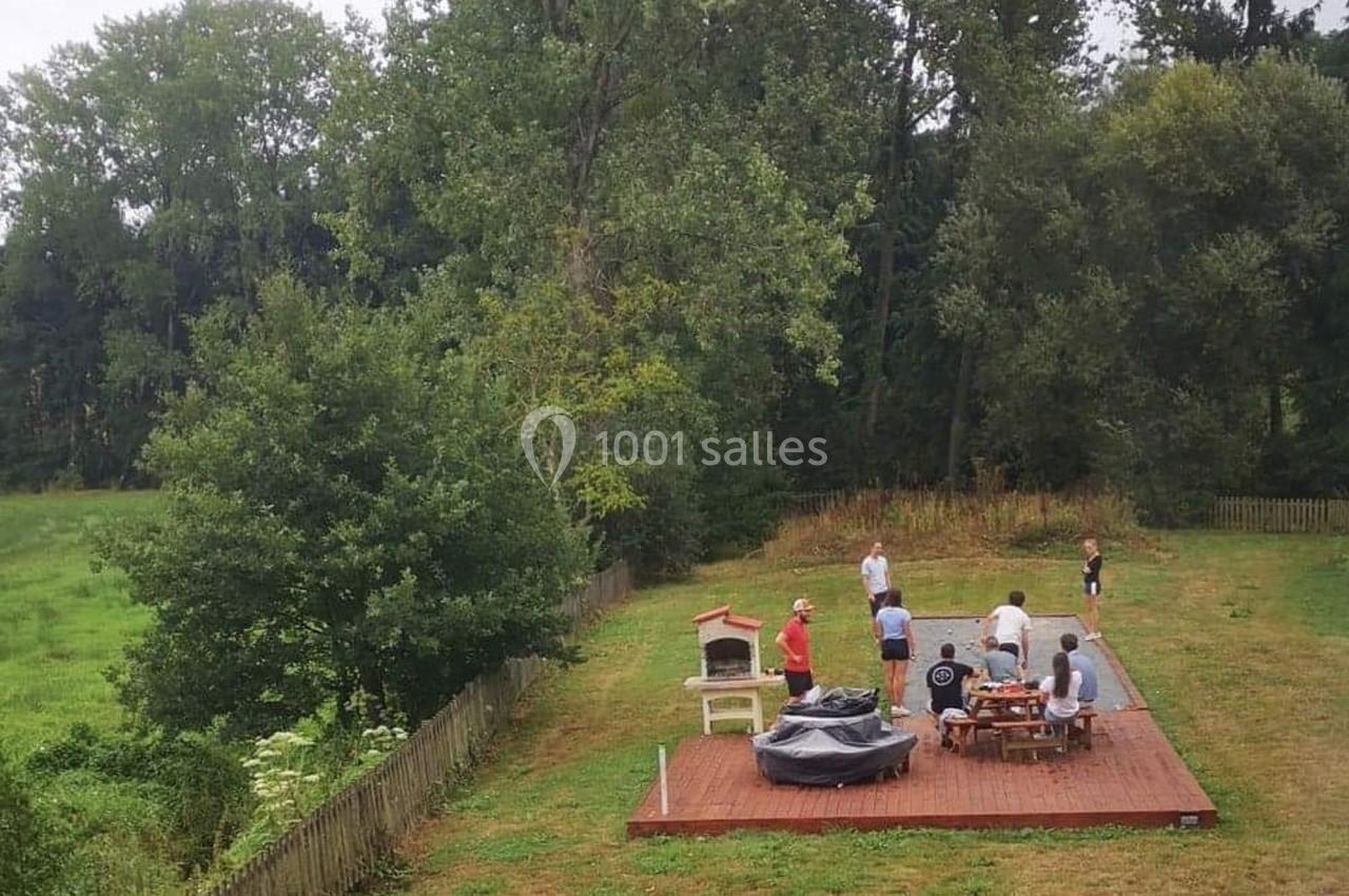 Des personnes discutent autour d'une table en bois sur une terrasse dans un jardin entouré d'arbres.