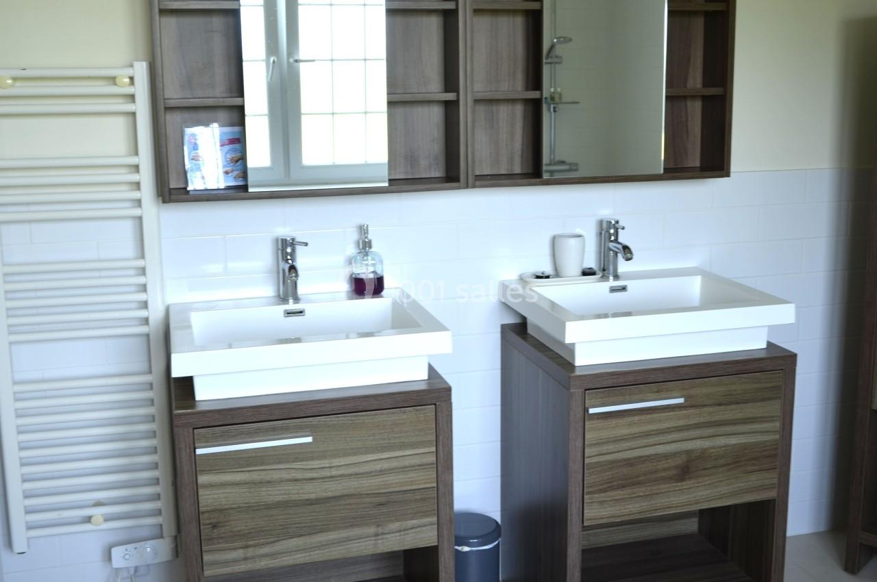 Deux lavabos avec meubles en bois, miroir, étagères ouvertes et radiateur mural dans une salle de bain lumineuse.