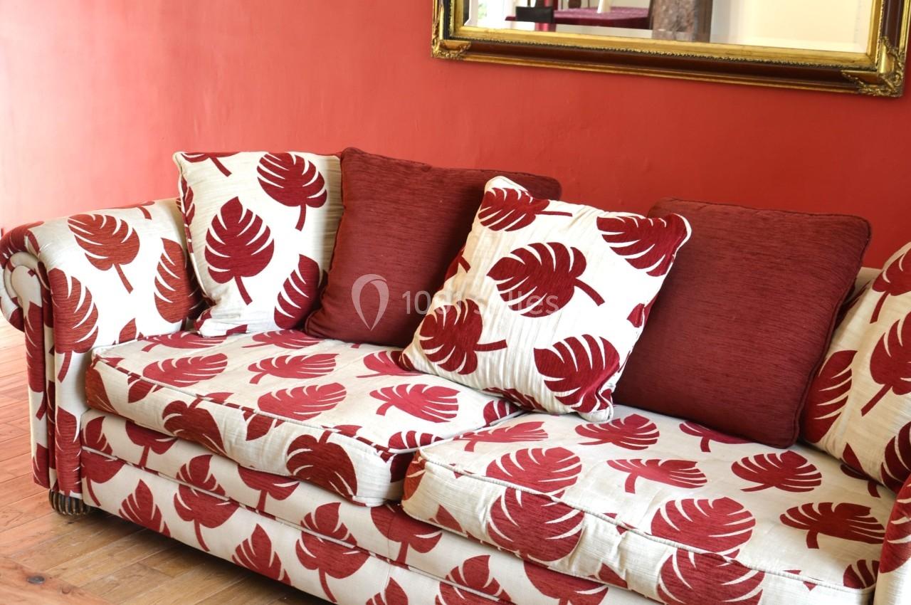 Canapé à motifs rouges et blancs devant un mur rouge, avec un miroir doré et une table basse en bois.