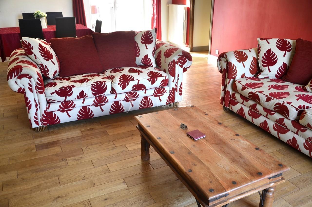 Deux canapés à motifs rouges et blancs entourent une table basse en bois dans un salon lumineux avec parquet.