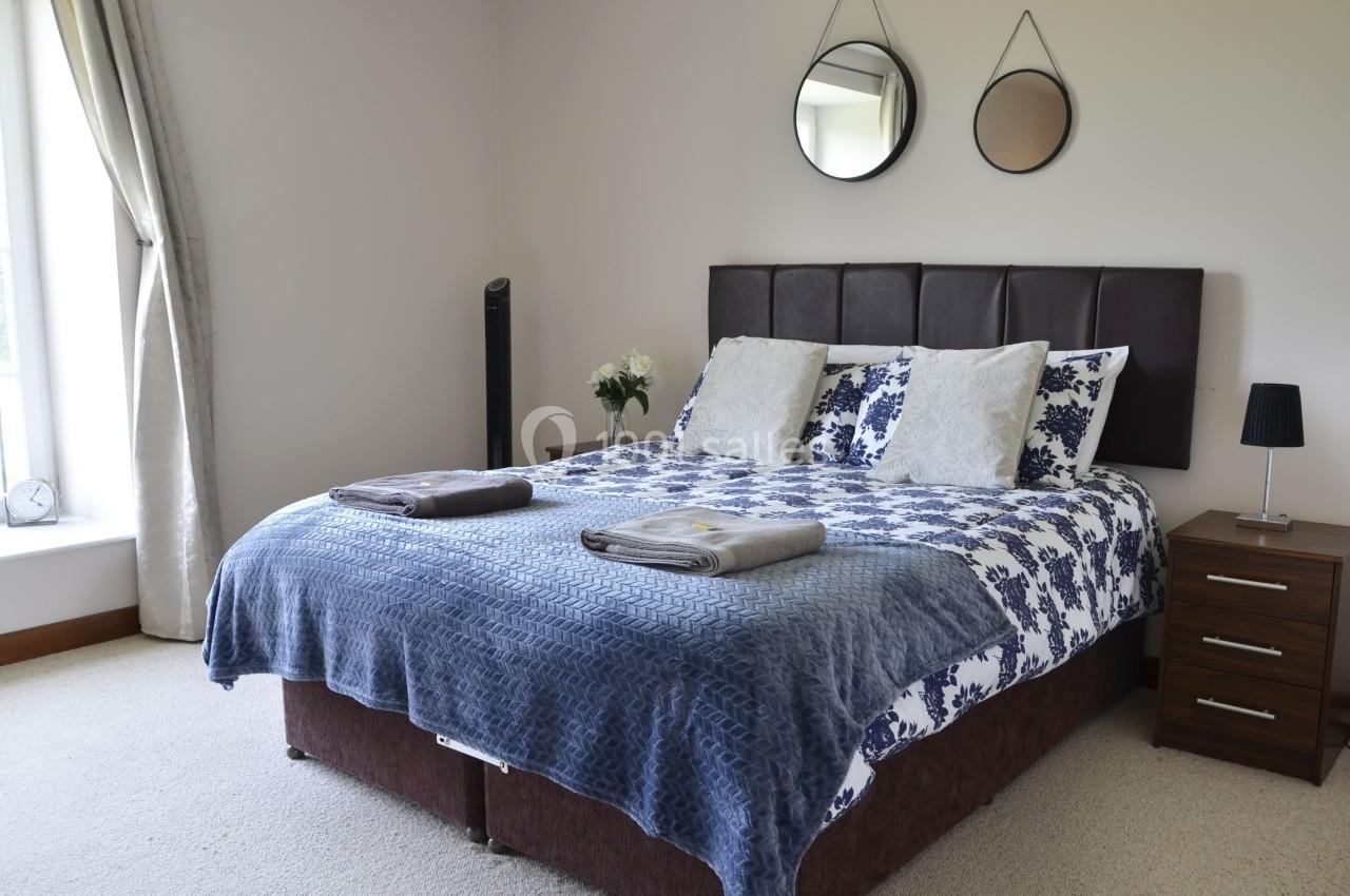 Chambre avec un lit double, linge de lit bleu et blanc, deux tables de chevet, miroirs ronds et une fenêtre lumineuse.