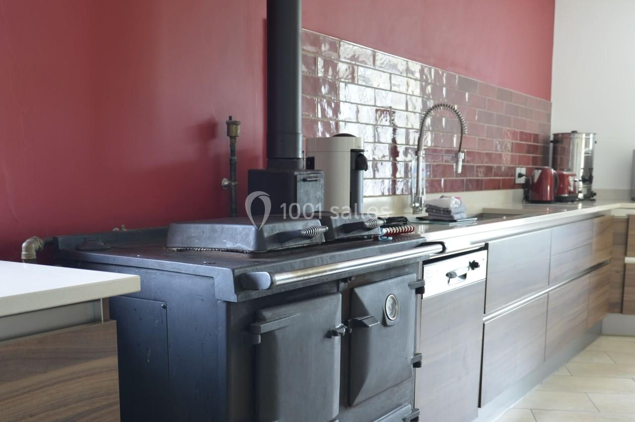 Cuisine moderne avec un poêle noir ancien, mur rouge, crédence en carrelage brillant et mobilier en bois.