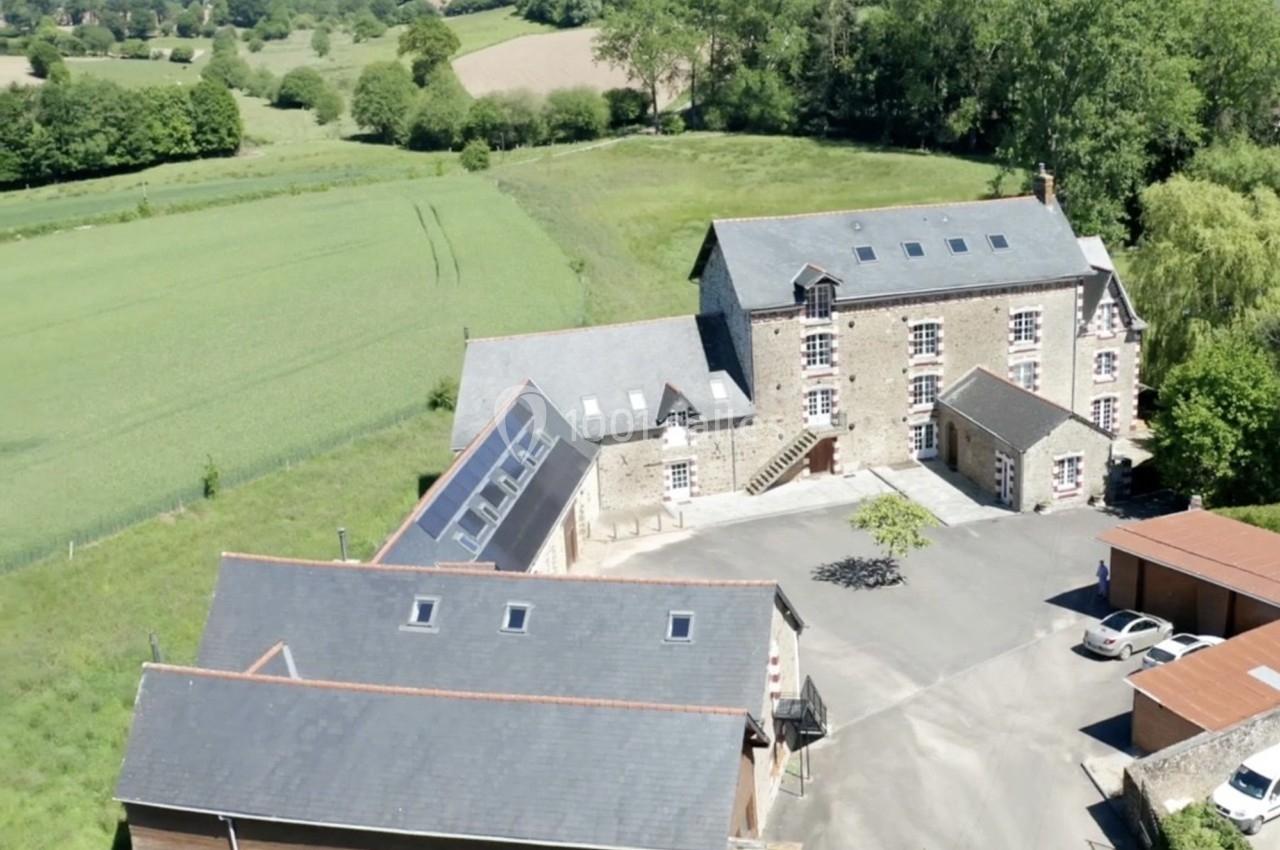 Vue aérienne d'un ensemble de bâtiments en pierre et en bois entourés de champs et de végétation.