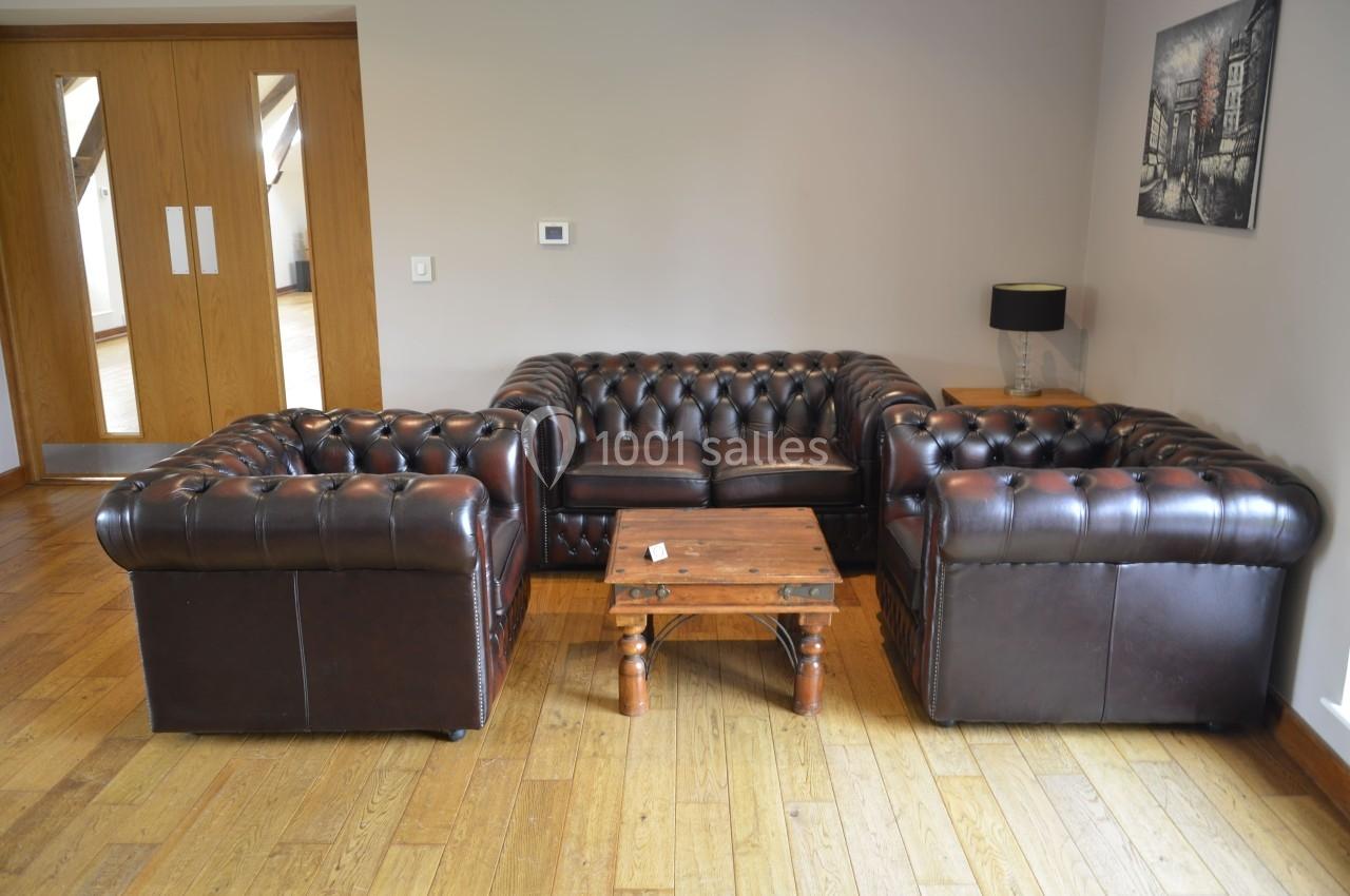 Canapé et fauteuils en cuir marron disposés autour d'une table basse en bois dans un salon au parquet clair.