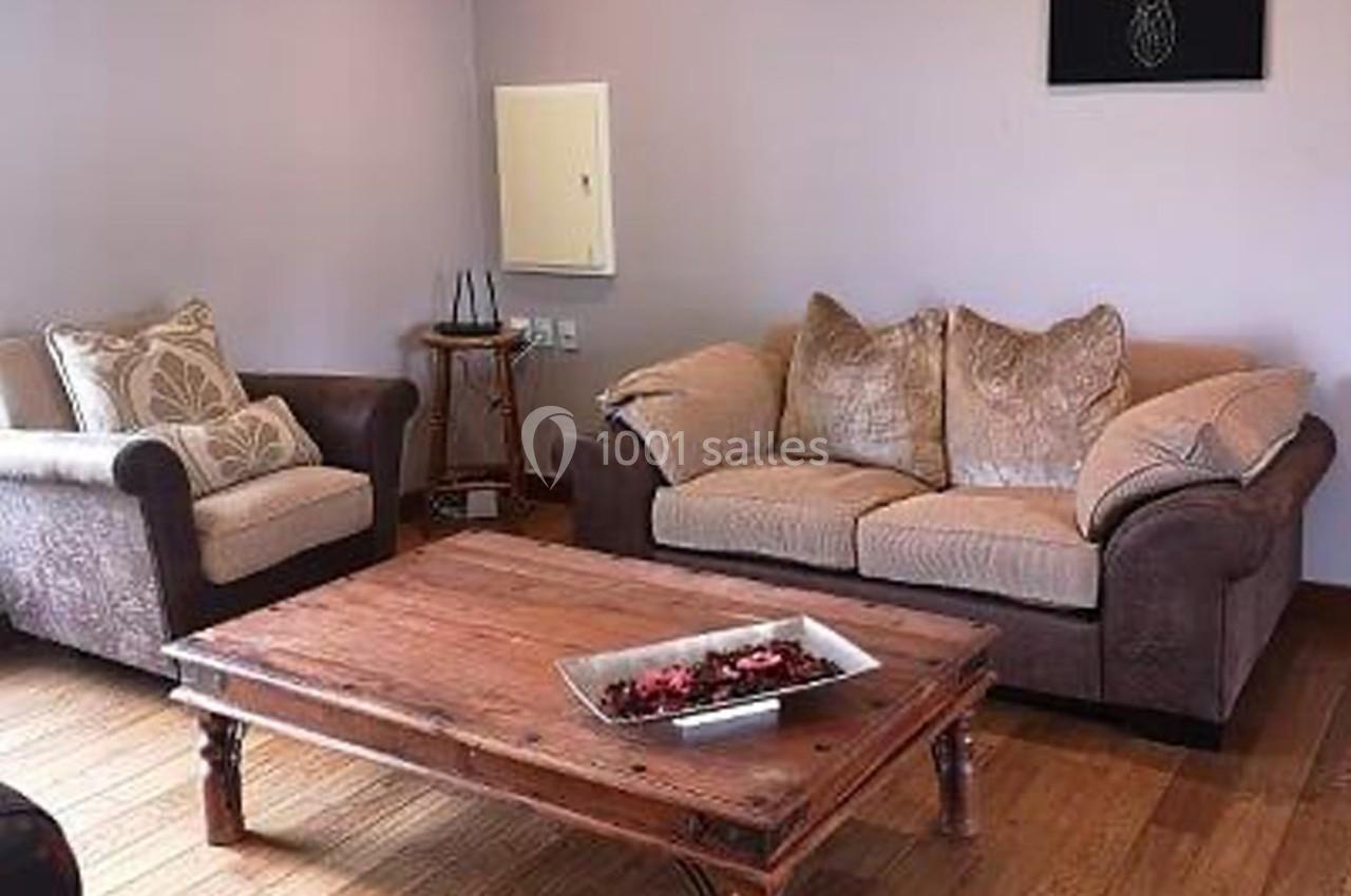 Salon avec canapé beige, fauteuil assorti, table basse en bois et décoration murale sur un sol en parquet.