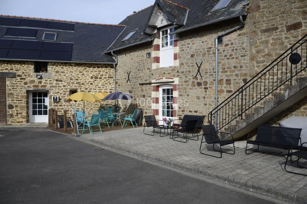 Cour d'une maison en pierre avec mobilier de jardin coloré, escaliers extérieurs et panneaux solaires sur le toit.