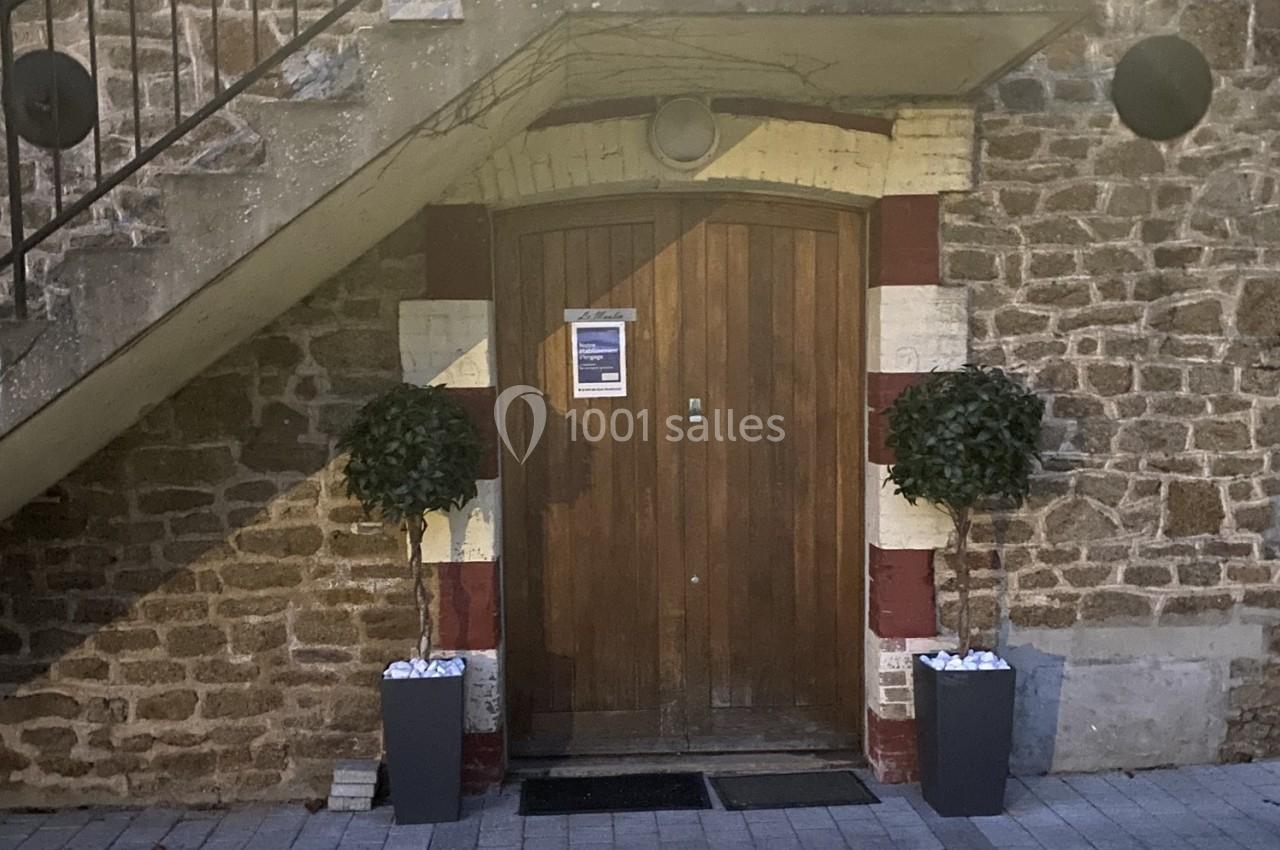 Porte en bois encadrée de briques rouges et blanches, flanquée de deux arbustes en pots, sous un escalier en pierre.