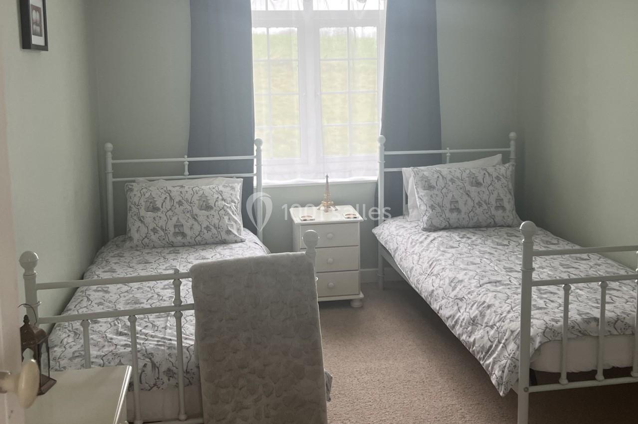 Deux lits simples avec linge de lit à motifs, une table de chevet et une fenêtre avec rideaux gris dans une chambre…