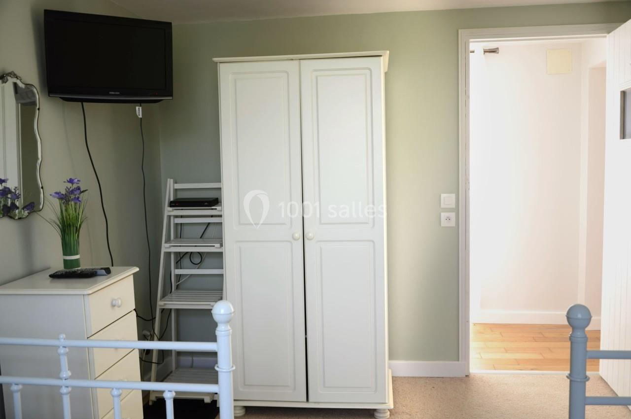 Armoire blanche dans une chambre lumineuse avec une télévision murale, une étagère et une porte ouverte sur un couloir.