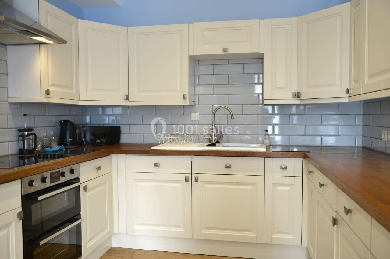 Cuisine moderne avec meubles blancs, plan de travail en bois, crédence en carreaux gris et évier en acier inoxydable.