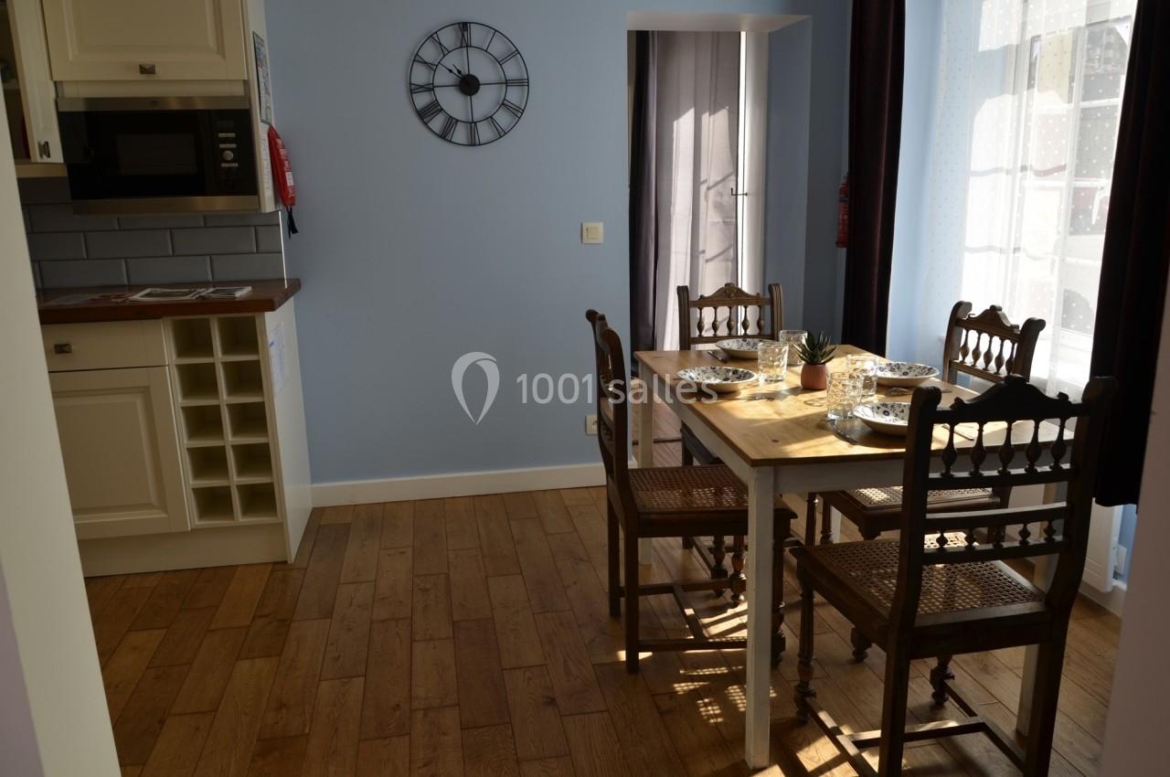 Cuisine lumineuse avec table en bois, chaises en bois sculpté, micro-ondes intégré et mur bleu clair.