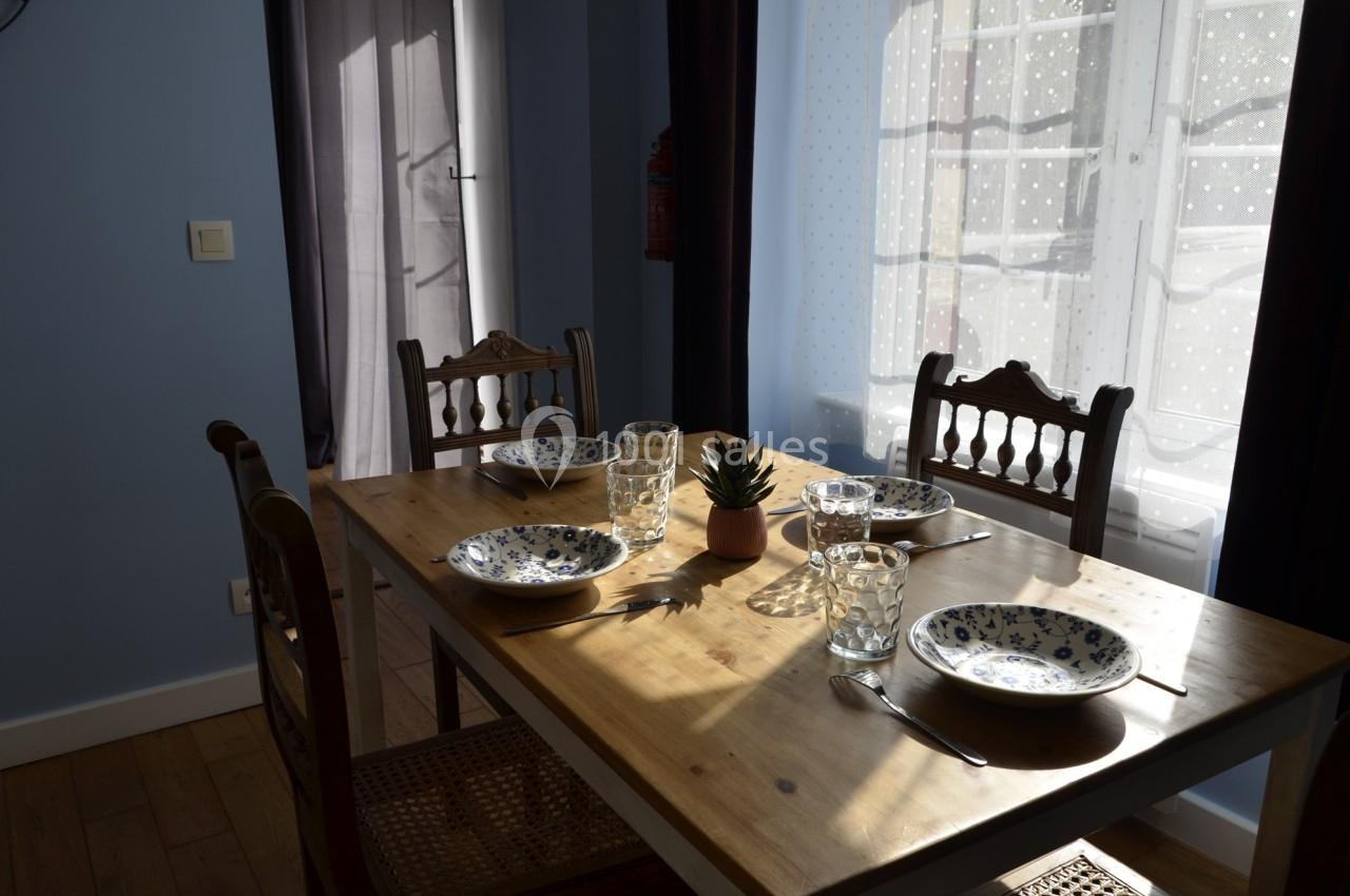 Table en bois avec quatre chaises, dressée avec des assiettes à motifs, des verres et une petite plante au centre.