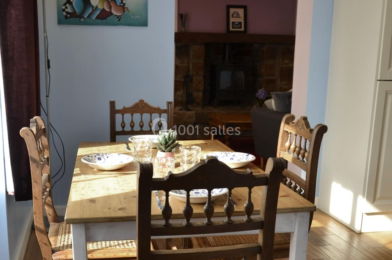 Table en bois dressée avec des assiettes et des verres, entourée de chaises, dans une pièce lumineuse avec un poêle en…