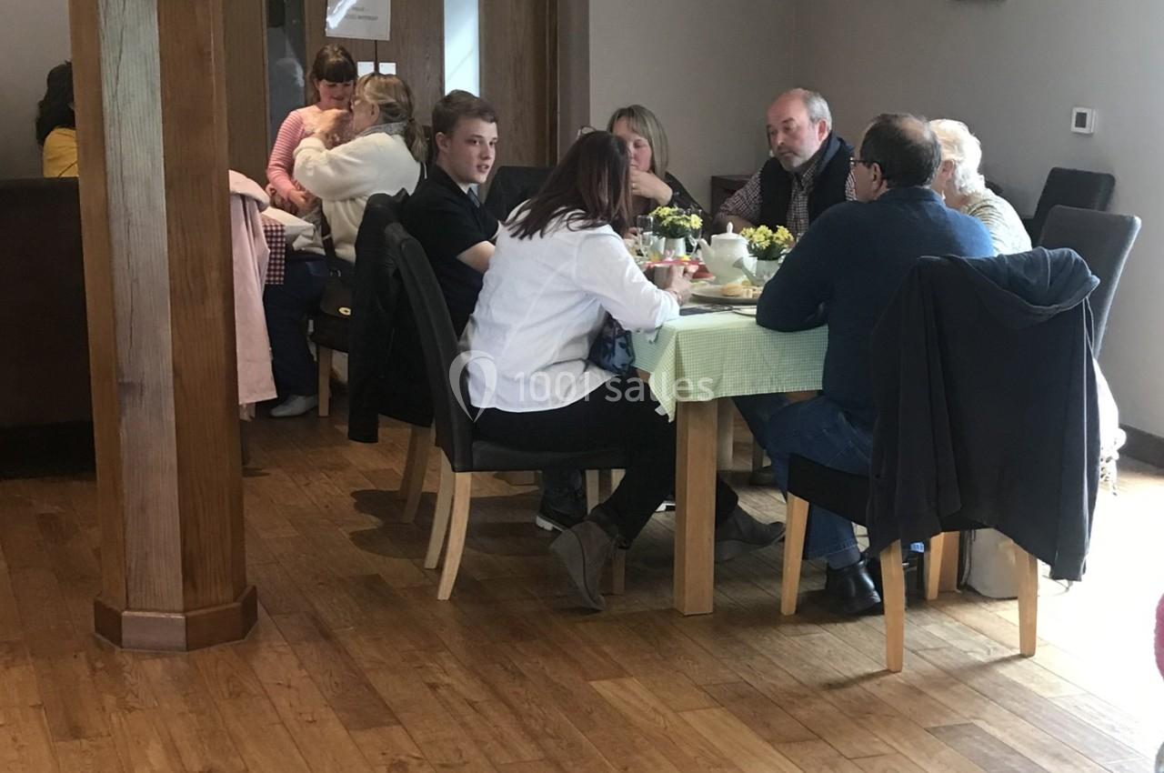 Des personnes assises autour de deux tables dans un intérieur lumineux, discutant et partageant un repas.