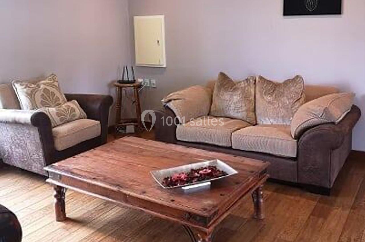 Salon avec un canapé, un fauteuil, une table basse en bois et un plateau décoratif, sur un sol en parquet.