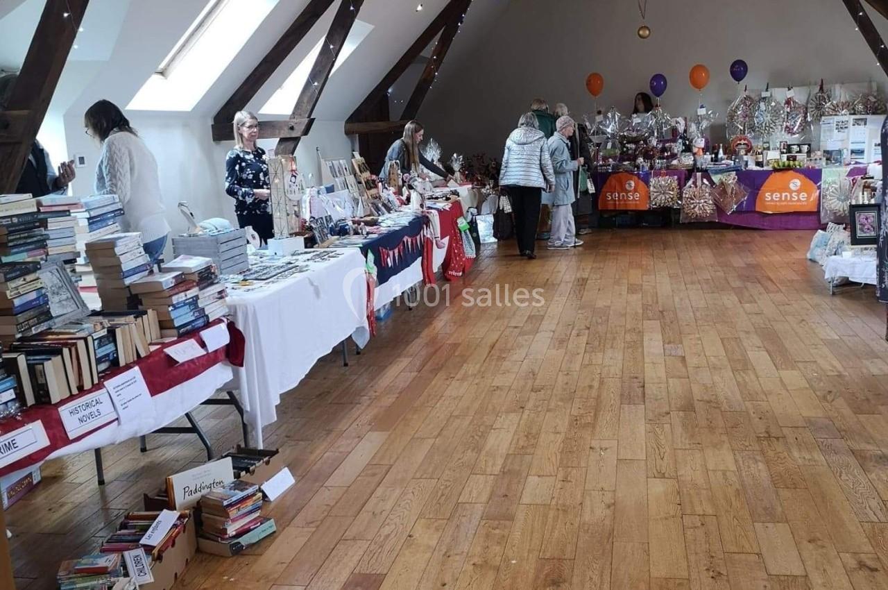 Salle avec des stands proposant des livres, décorations et articles divers, plusieurs personnes en train de regarder.