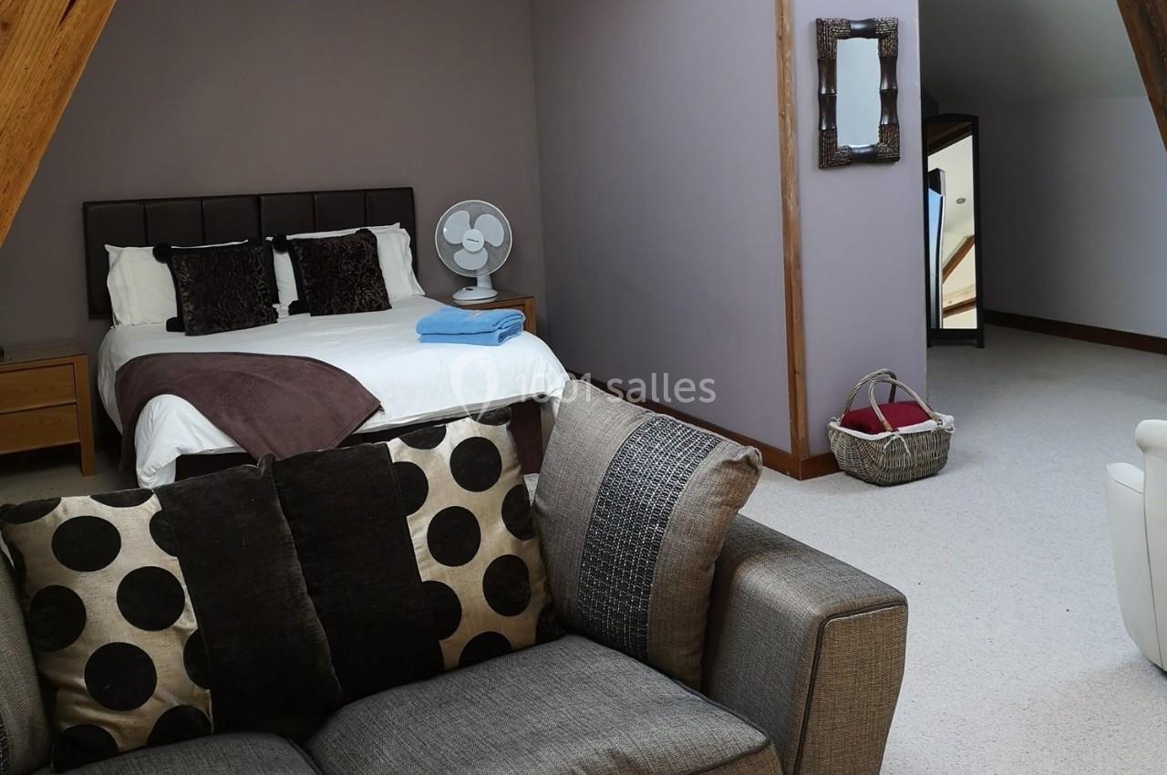 Chambre mansardée avec lit double, canapé, ventilateur sur une table de chevet et panier posé au sol.