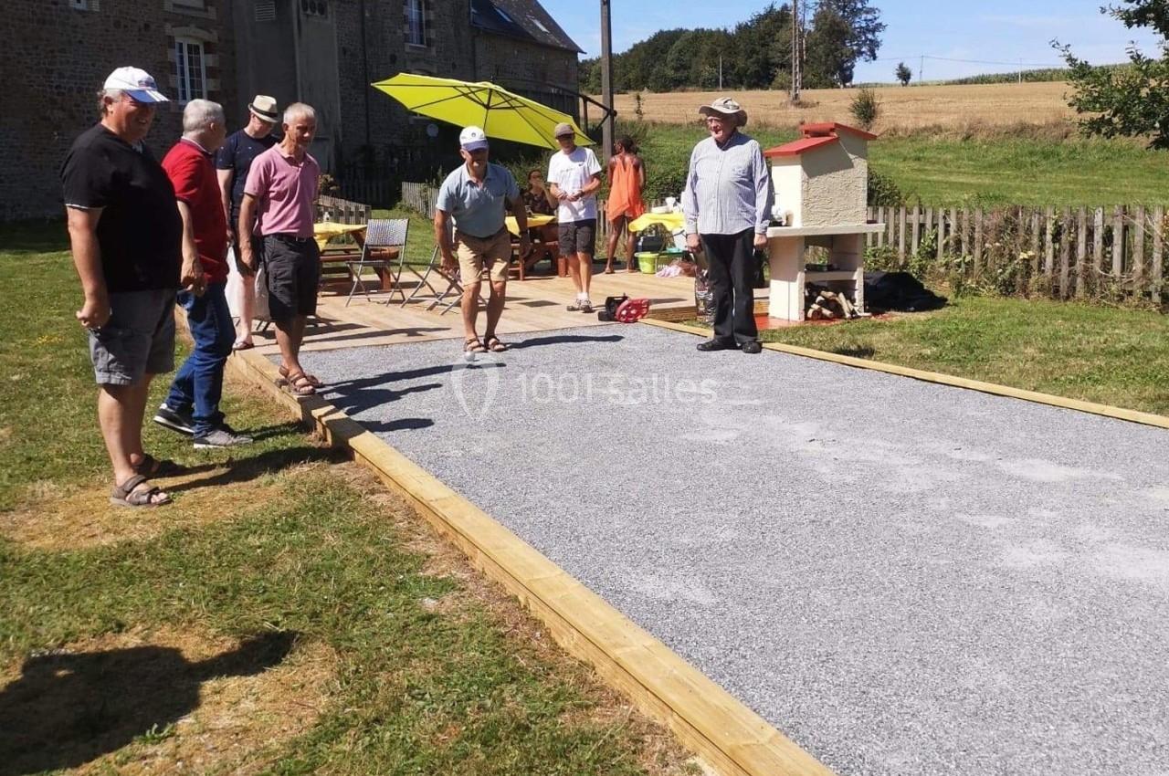 Des personnes jouent à la pétanque sur un terrain aménagé en plein air, entouré de verdure et de bâtiments ruraux.