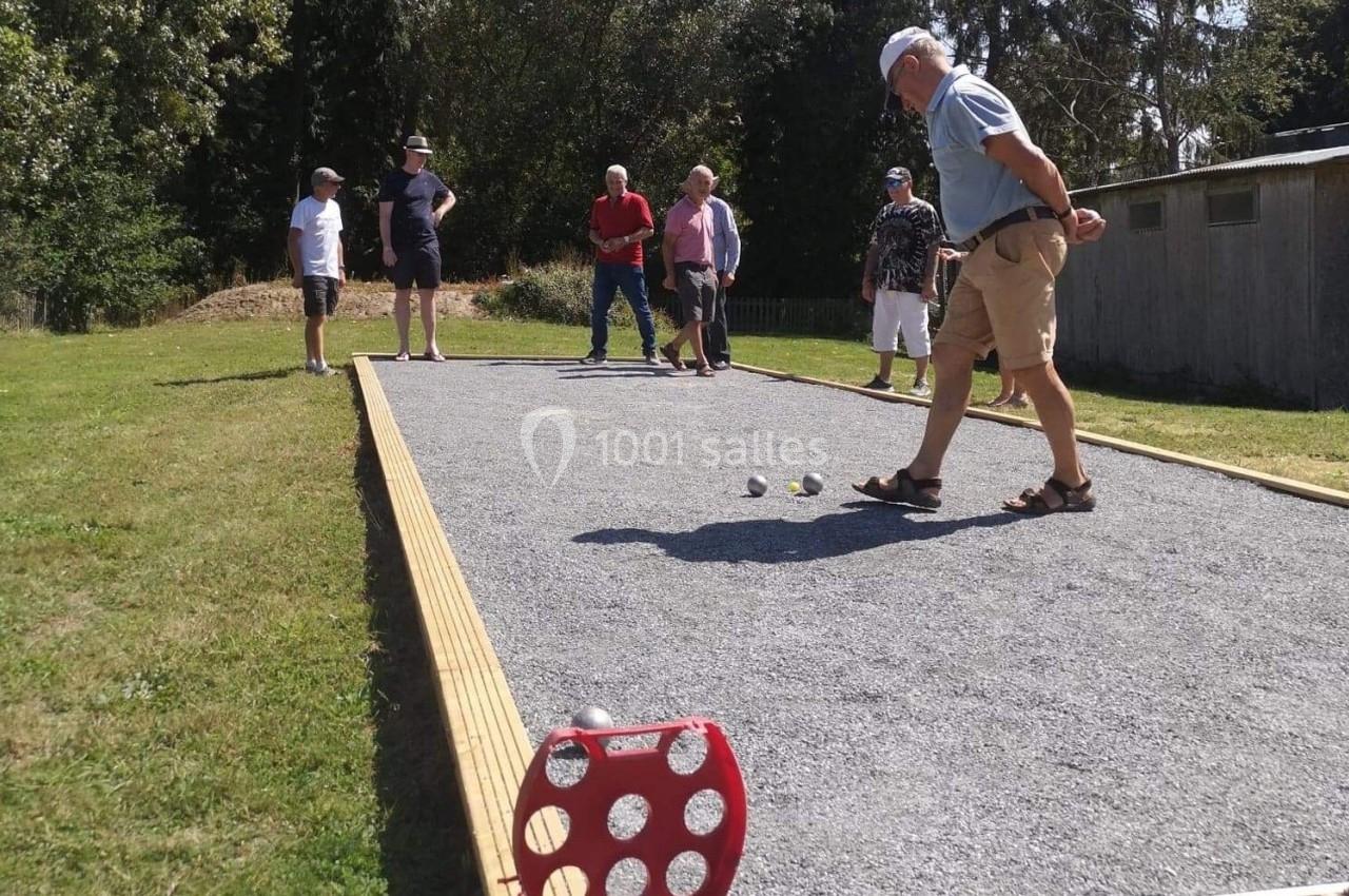 Des personnes jouent à la pétanque sur un terrain en gravier, entourées de verdure et d'arbres.