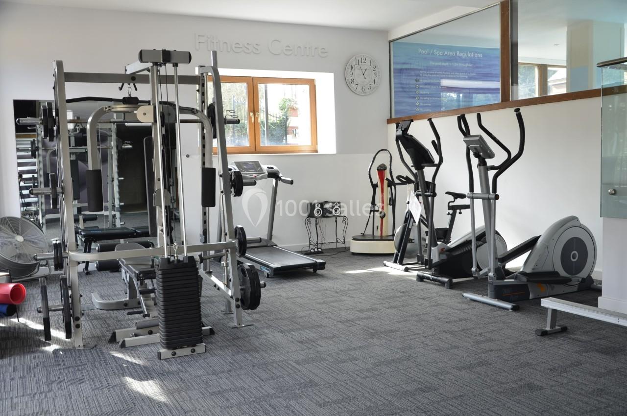 Salle de sport lumineuse avec équipements de musculation, tapis de course et vélos elliptiques.