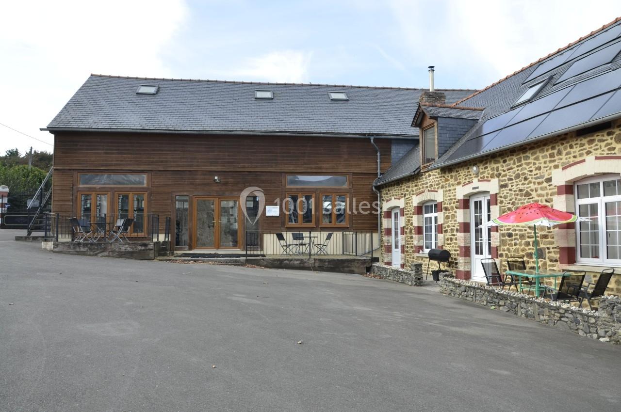 Bâtiment en pierre et bois avec terrasse, chaises, parasol et panneaux solaires sur le toit, sous un ciel dégagé.