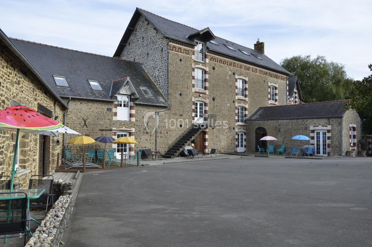 Bâtiment en pierre avec enseigne ’Minoterie de la Quentinière’, entouré de parasols colorés sur une cour pavée.