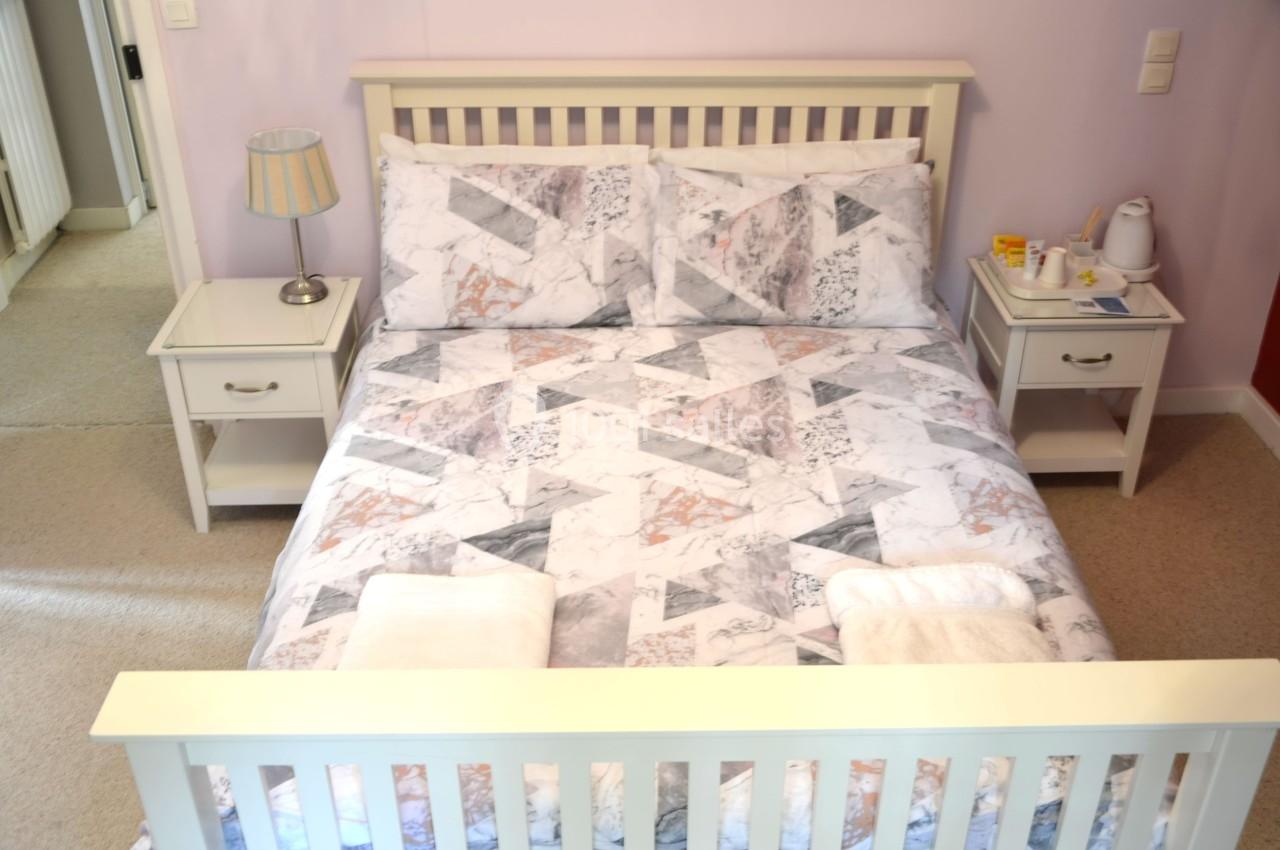 Lit double avec draps à motifs géométriques, deux tables de chevet, lampe, serviettes pliées et plateau avec boissons.