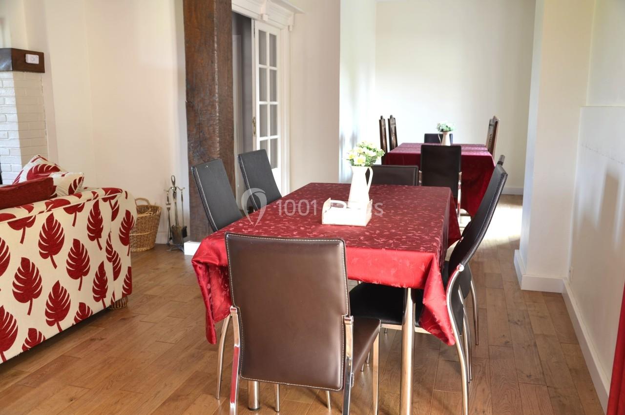 Salle à manger lumineuse avec table rectangulaire recouverte d'une nappe rouge, entourée de chaises en cuir sombre.