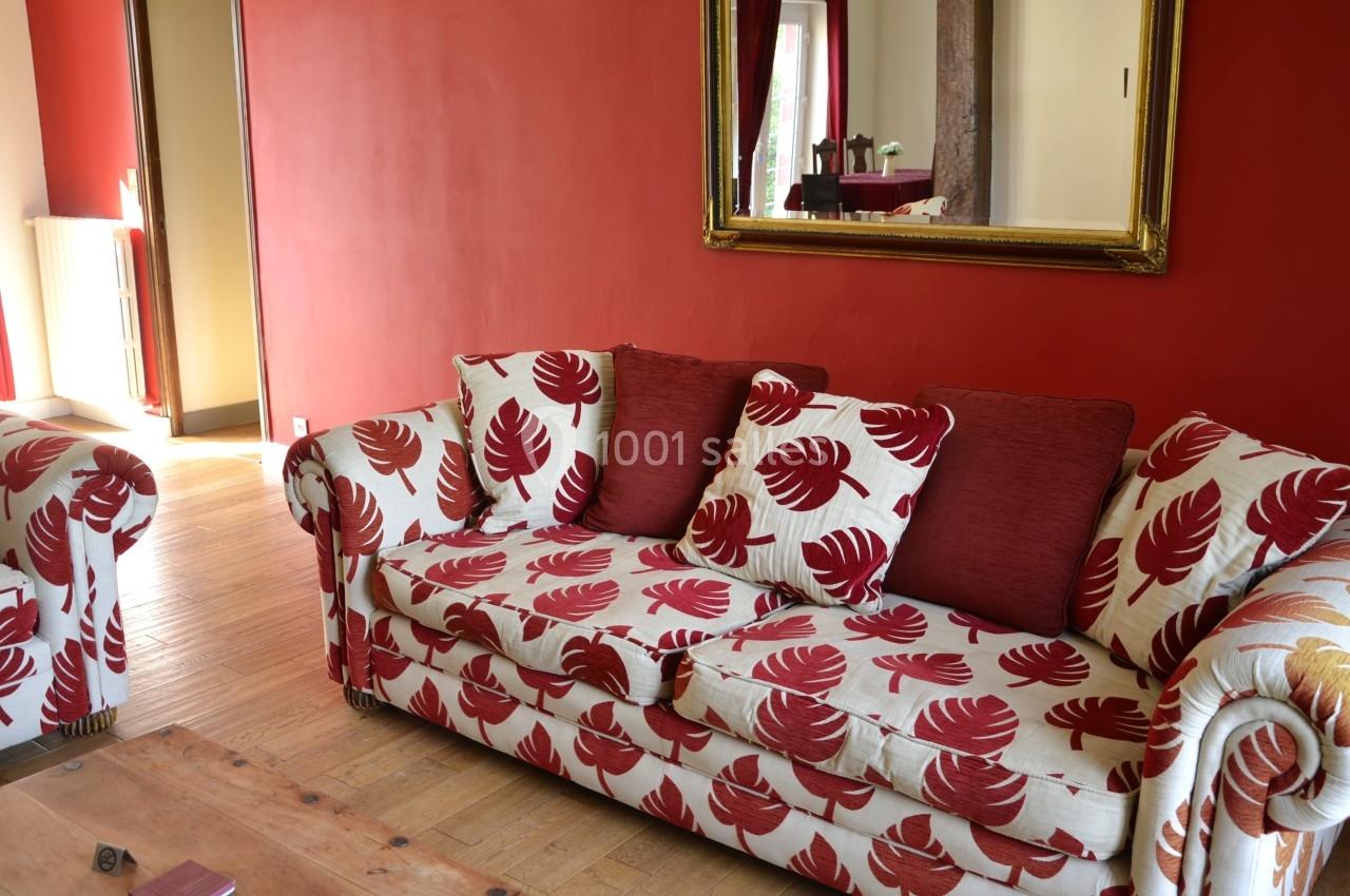 Canapé à motifs rouges et blancs avec coussins assortis, placé dans un salon aux murs rouges et parquet en bois.