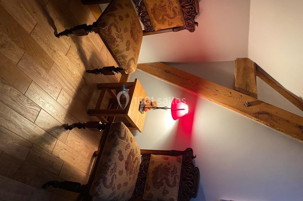 Deux chaises en bois sculpté avec assises rembourrées entourent une petite table éclairée par une lampe rouge.